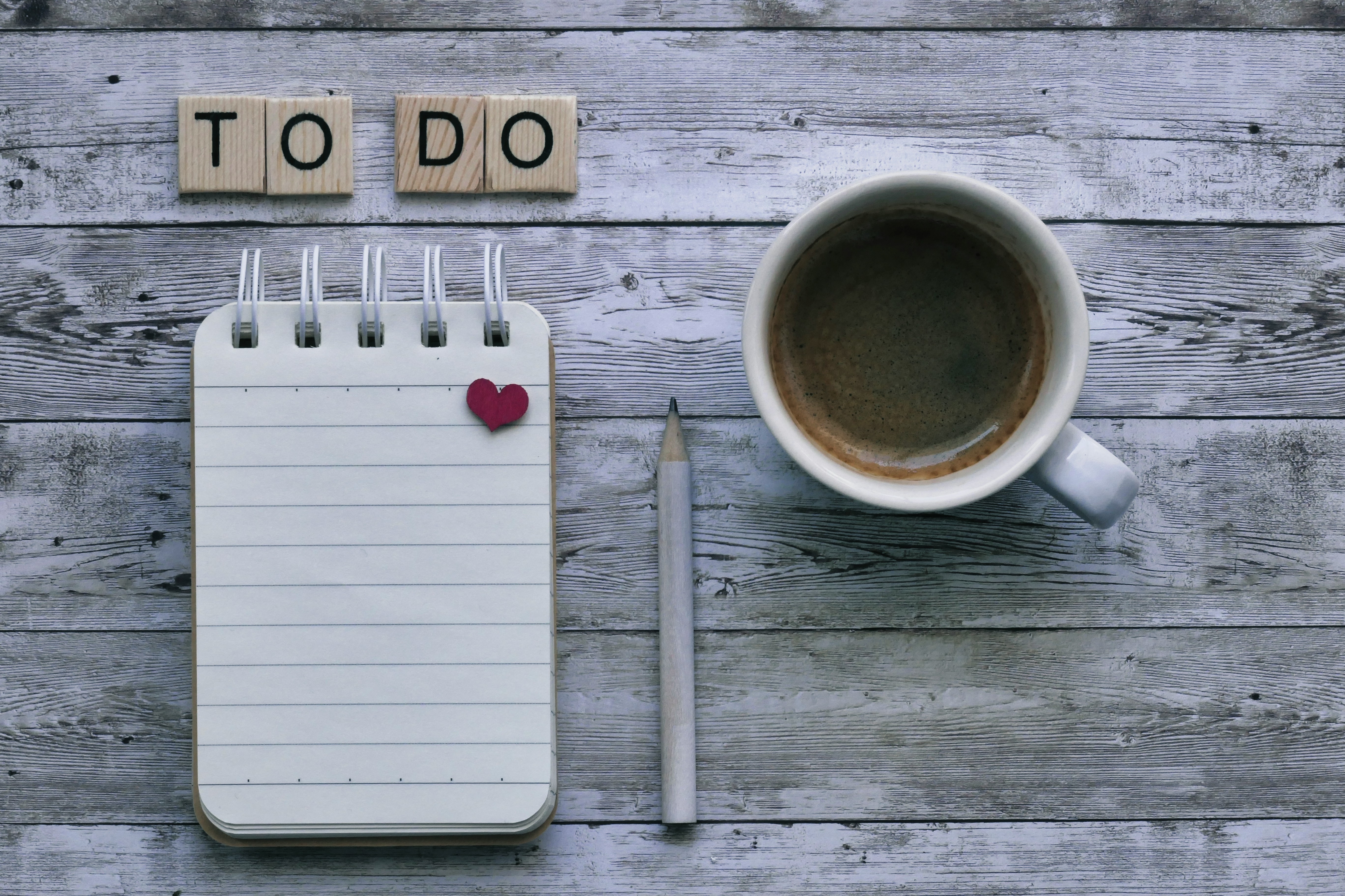 Notepad, pencil, and coffee cup on a wooden desk with 'To Do' scrabble tiles — planning checklist before buying a home
